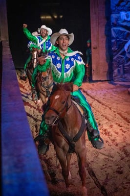 Horse riders wearing green enter the arena atop brown horses