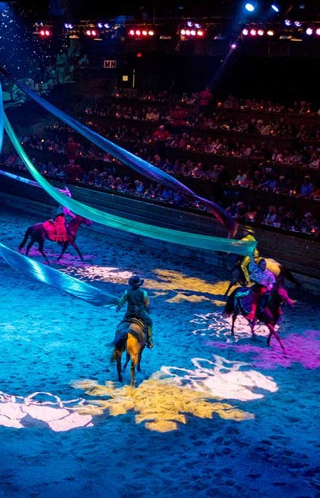 Brightly colored lights shine on horses with riders holding large streamers