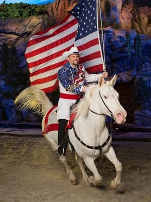 Stampede performer riding a horse and carrying an American flag